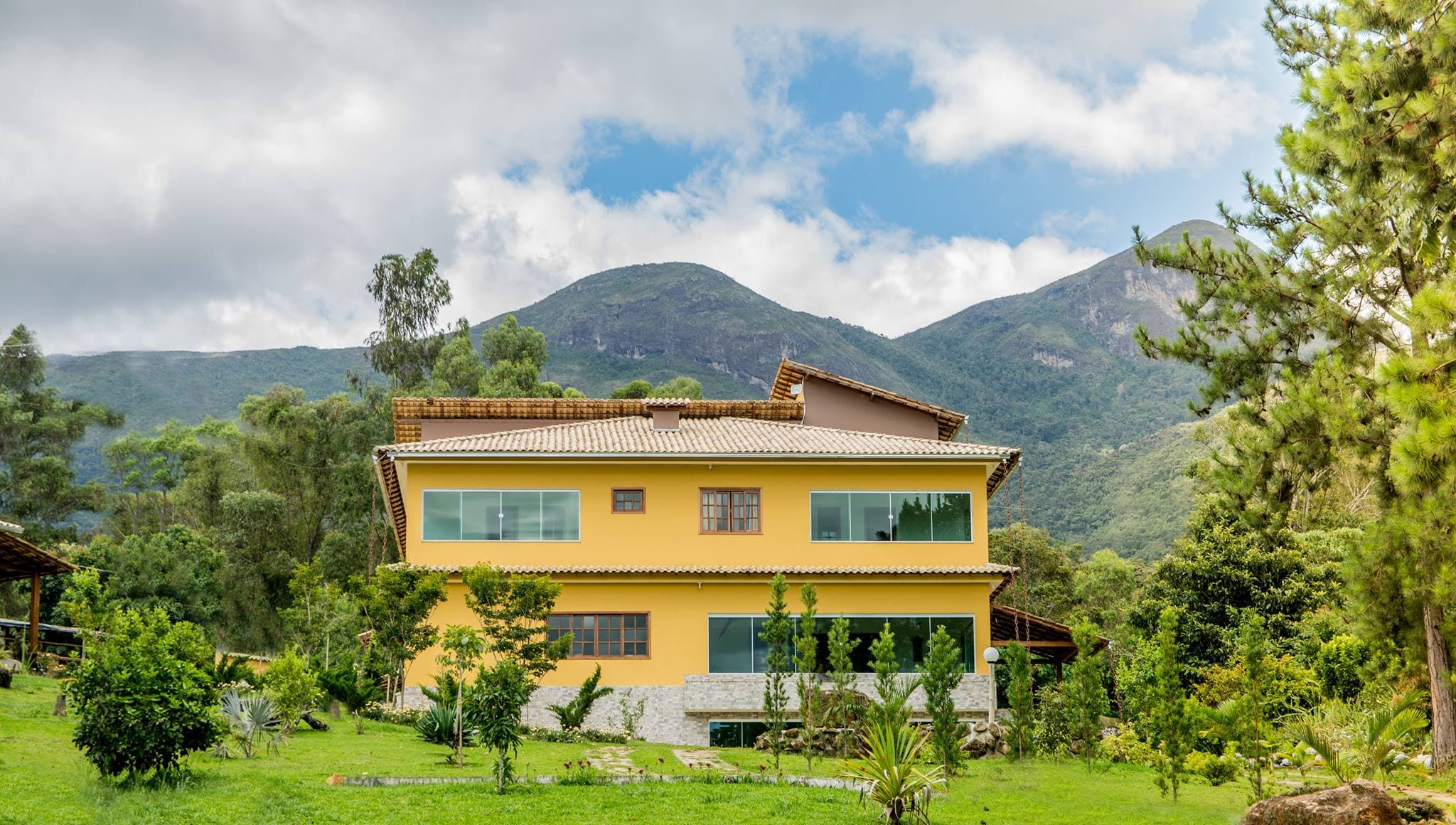Fachada amarela da Pousada Alto das Colinas com a serra do Caparaó ao fundo